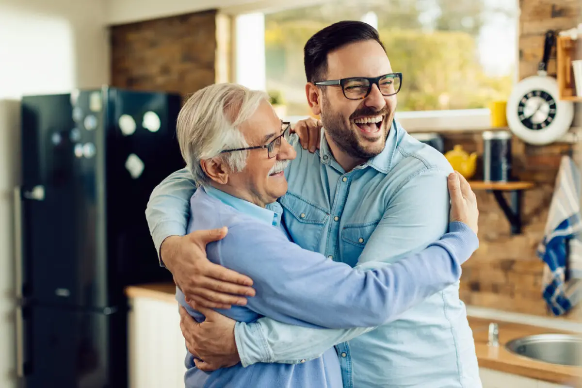 Cheerful mid adult man and his senior father embracing in the ki, Cheerful mature man and his adult son embracing while greeting in the kitchen.