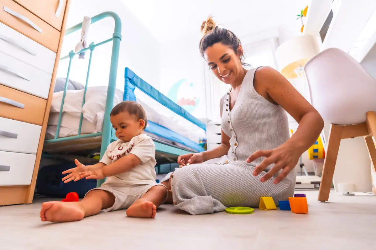 Young Caucasian mother playing with her in the room with toys., Young Caucasian mother playing with her in the room with toys. Baby less than a year learning the first lessons of her mother. Mother playing with her son playing sitting on the floor